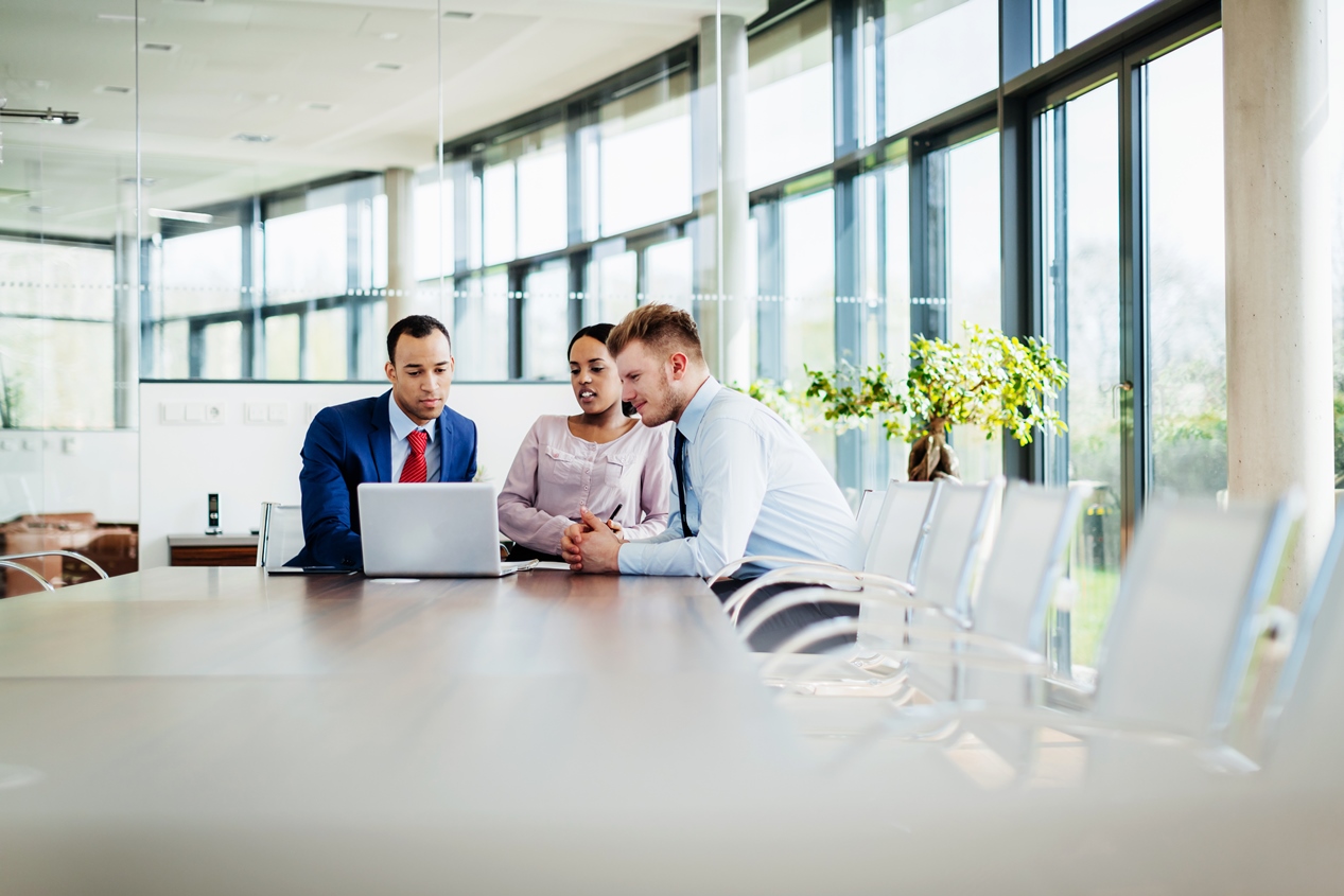 Ein Meeting von drei Geschäftsleuten, die an einem Konferenztisch in einem modernen Büro sitzen.	
	