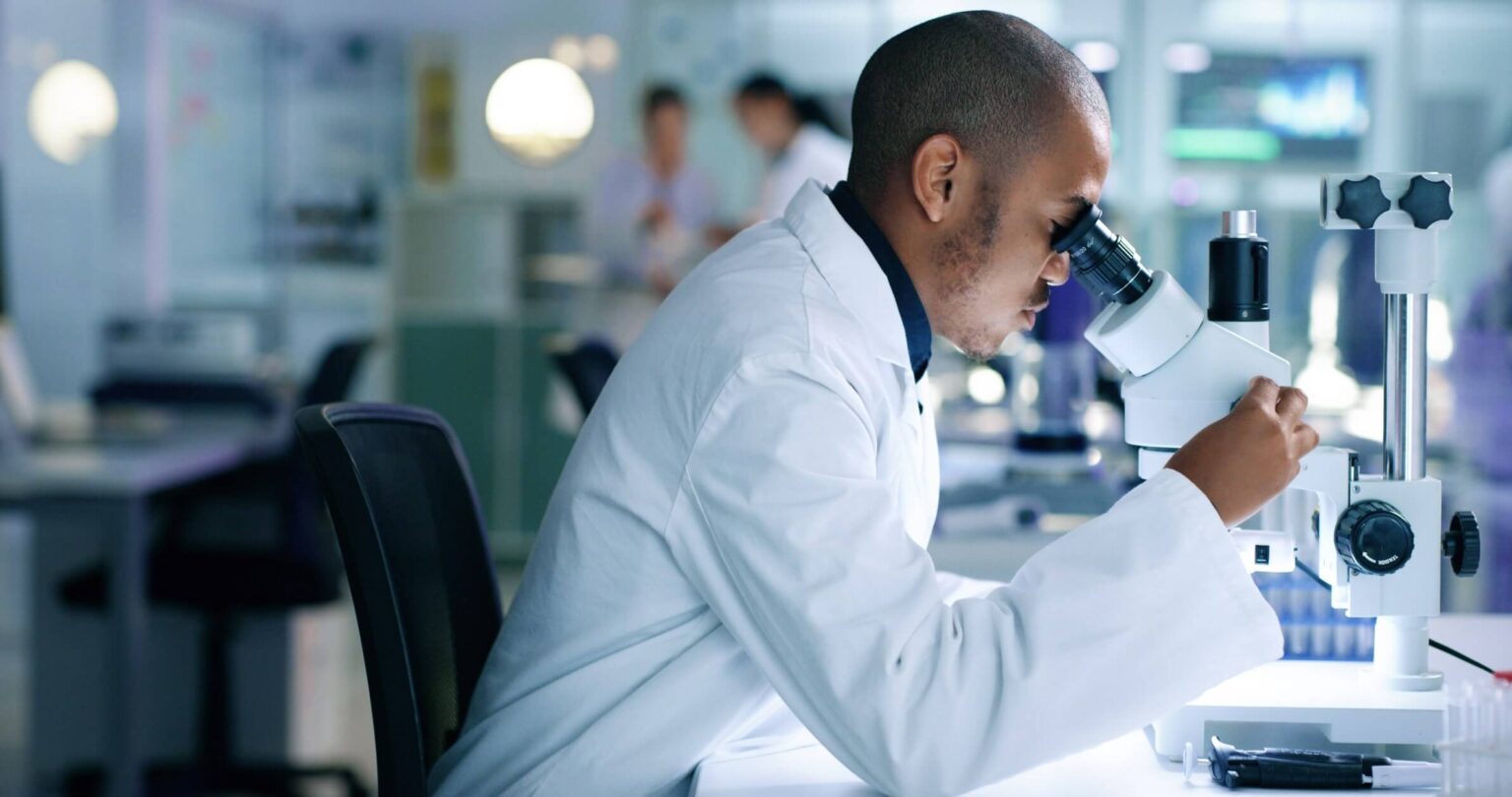 Ein Wissenschaftler schaut durch ein Mikroskop im Labor und verwendet das Labor-Informations-Management-System von STARLIMS