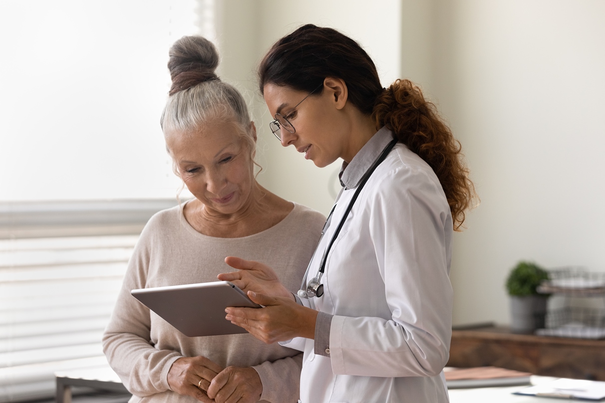 Professionnel de santé montrant les résultats des tests sur l’écran d’une tablette à une patiente âgée.